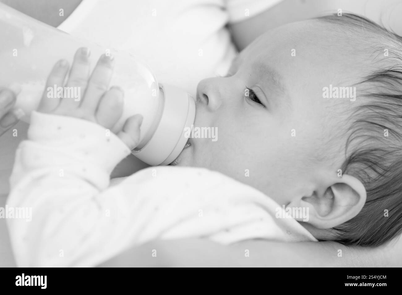 Portrait en gros plan noir et blanc de mignon bébé de 3 mois buvant du lait de la bouteille Banque D'Images