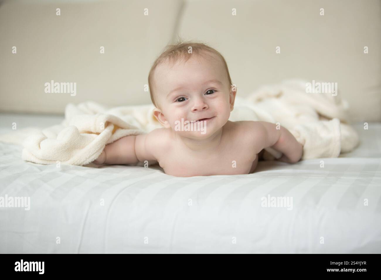Mignon petit garçon allongé sur le lit sous une grande couverture blanche Banque D'Images