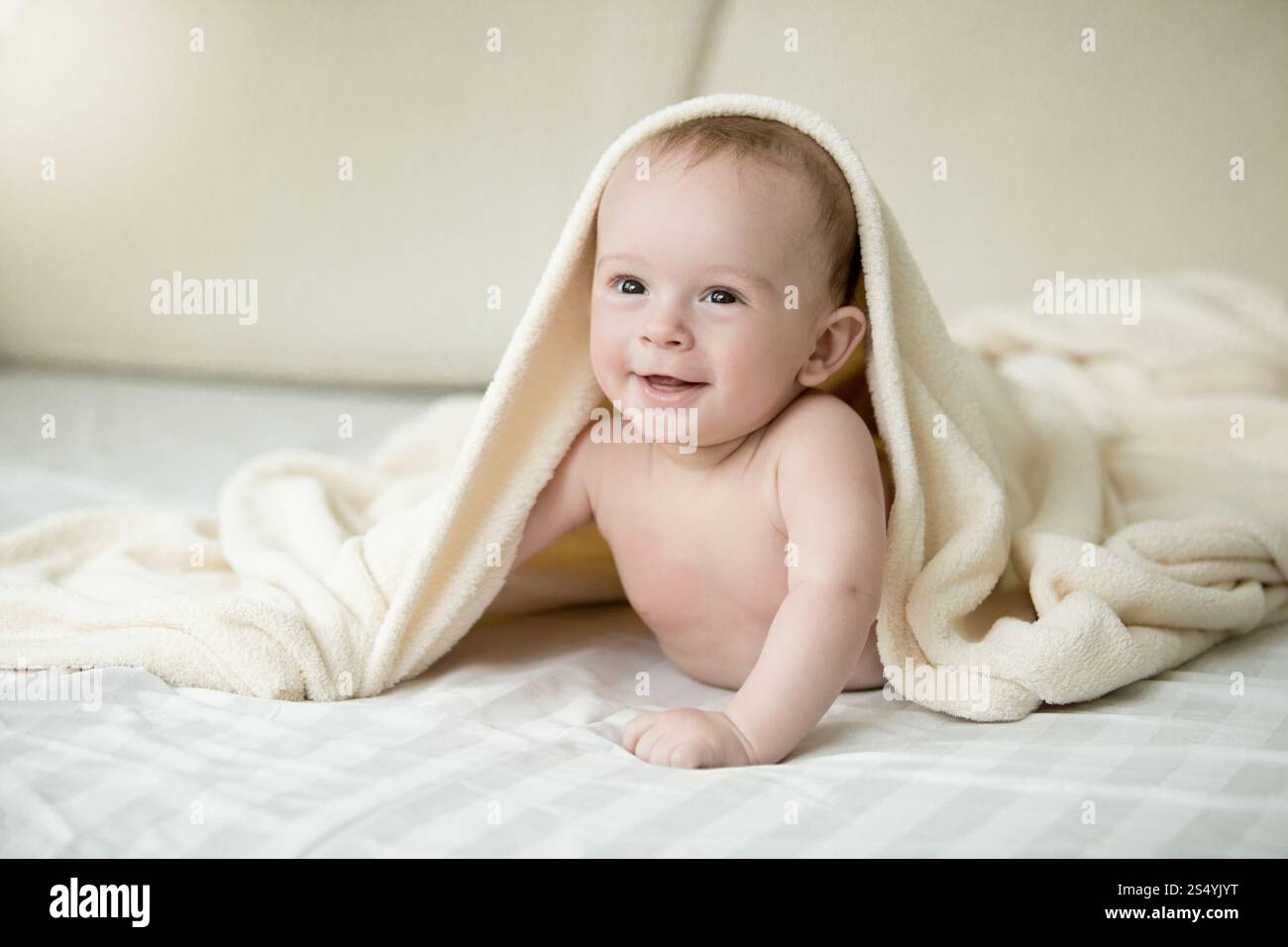 Portrait de bébé garçon surpris couché sous une couverture sur le lit Banque D'Images