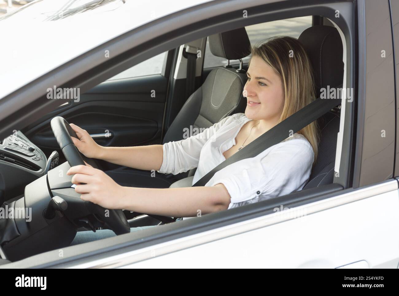 Jeune femme souriante conduisant une voiture et regardant la route Banque D'Images