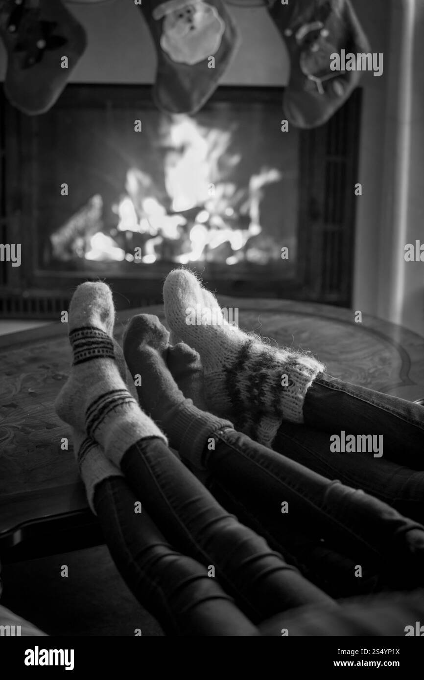 Image en noir et blanc de pieds de famille dans des chaussettes en laine se réchauffant à la cheminée à la veille de Noël Banque D'Images Image en noir et blanc de pieds de famille dans des chaussettes en laine se réchauffant à la cheminée à la veille de Noël Banque D'Images