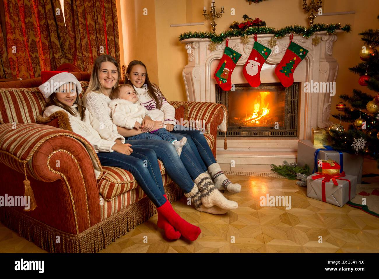 Mère assise avec ses filles sur le canapé salon à côté de la cheminée en feu à Noël Banque D'Images Mère assise avec ses filles sur le canapé salon à côté de la cheminée en feu à Noël Banque D'Images