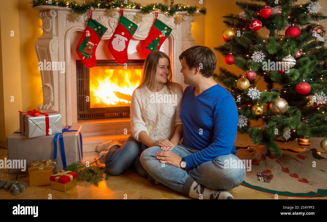 Jeune couple assis sur le sol à la cheminée en feu et donnant des cadeaux de Noël Banque D'Images Jeune couple assis sur le sol à la cheminée en feu et donnant des cadeaux de Noël Banque D'Images