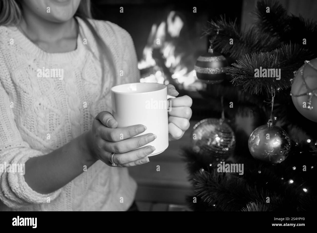 Gros plan image en noir et blanc d'une femme assise à la cheminée en feu avec une tasse de thé Banque D'Images