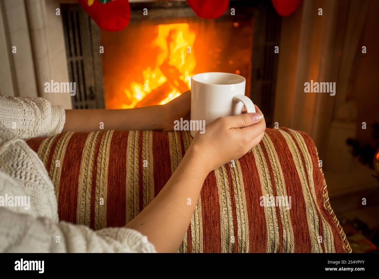 Image d'une femme assise sur un canapé à la cheminée et tenant une tasse de thé Banque D'Images Image d'une femme assise sur un canapé à la cheminée et tenant une tasse de thé Banque D'Images