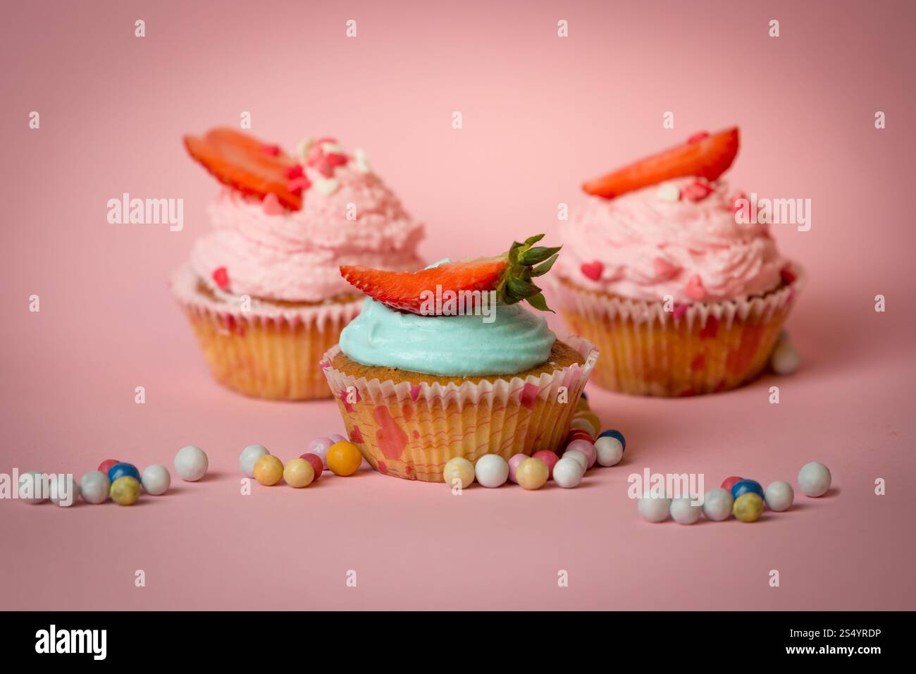 Trois cupcakes colorés avec des fraises sur fond rose avec des bonbons Banque D'Images