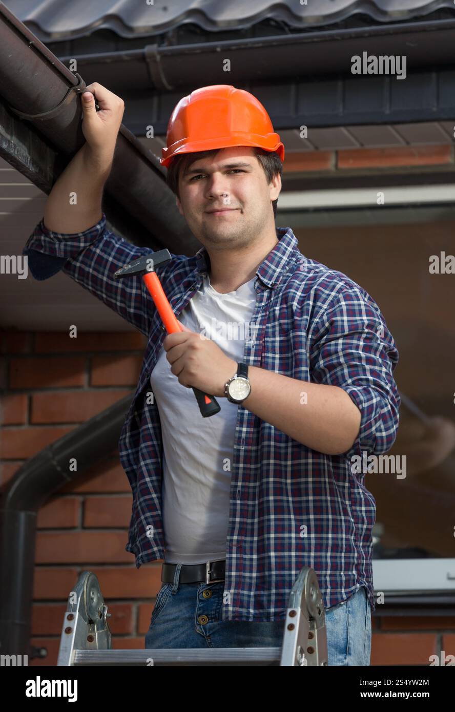 Jeune menuisier en casque dur examinant le toit de la maison Banque D'Images