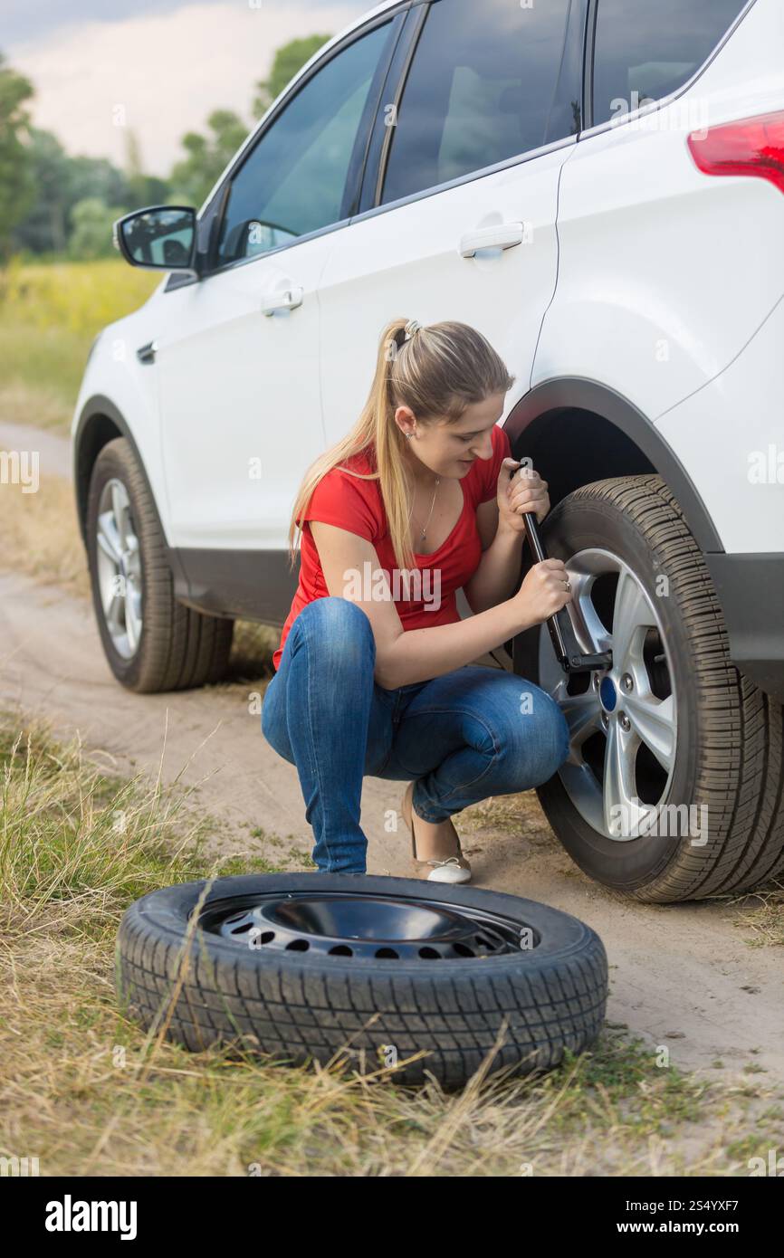 Femme dévissant des écrous sur la roue plate de voiture au champ Banque D'Images