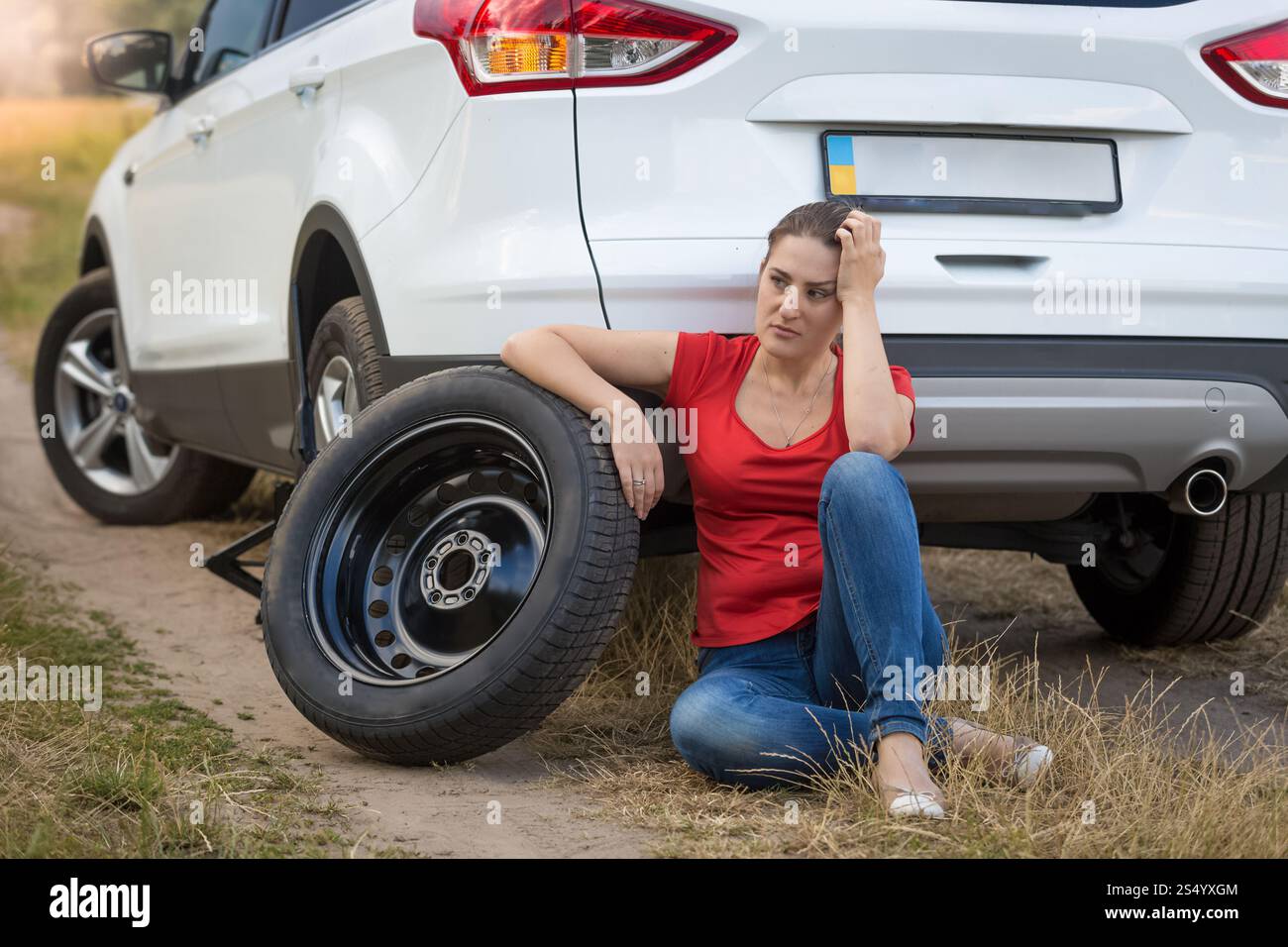 Femme assise à côté de la voiture avec un pneu crevé et attendant de l'aide Banque D'Images
