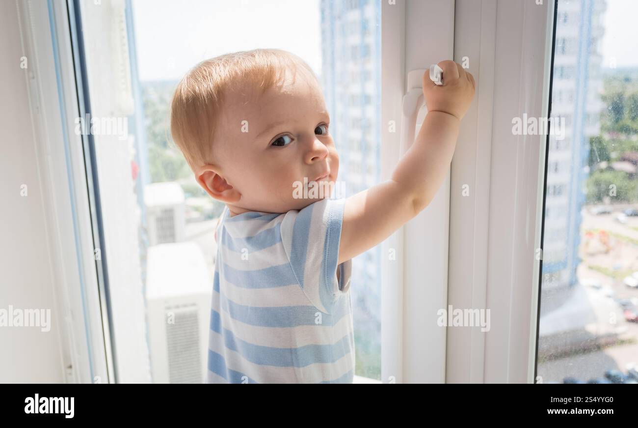 Bébé garçon tirant par la poignée de la fenêtre. La notion d'enfant en danger Banque D'Images