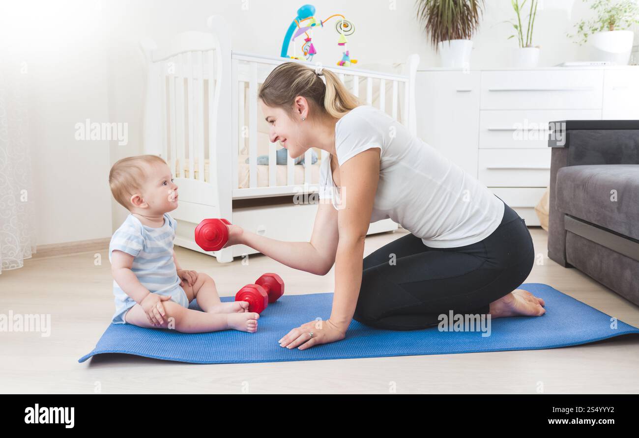 Mère souriante faisant de l'exercice physique avec son bébé sur le sol au salon Banque D'Images