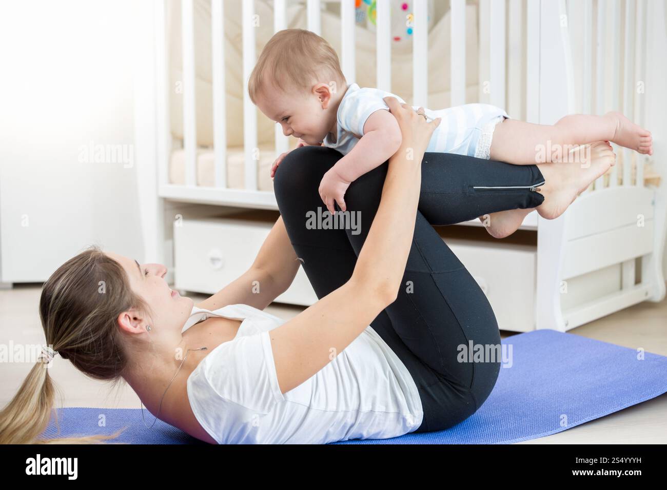 Femme souriante faisant de l'exercice de yoga avec son bébé dans le salon Banque D'Images