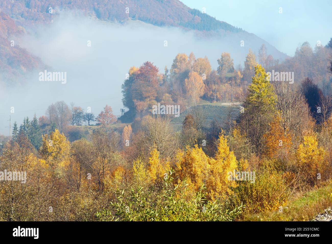 Paysage des montagnes des Carpates d'automne avec des arbres multicolores et un petit hameau sur la pente, et nuage brumeux au-dessus (district de Rakhiv, Transcarpathie, Banque D'Images
