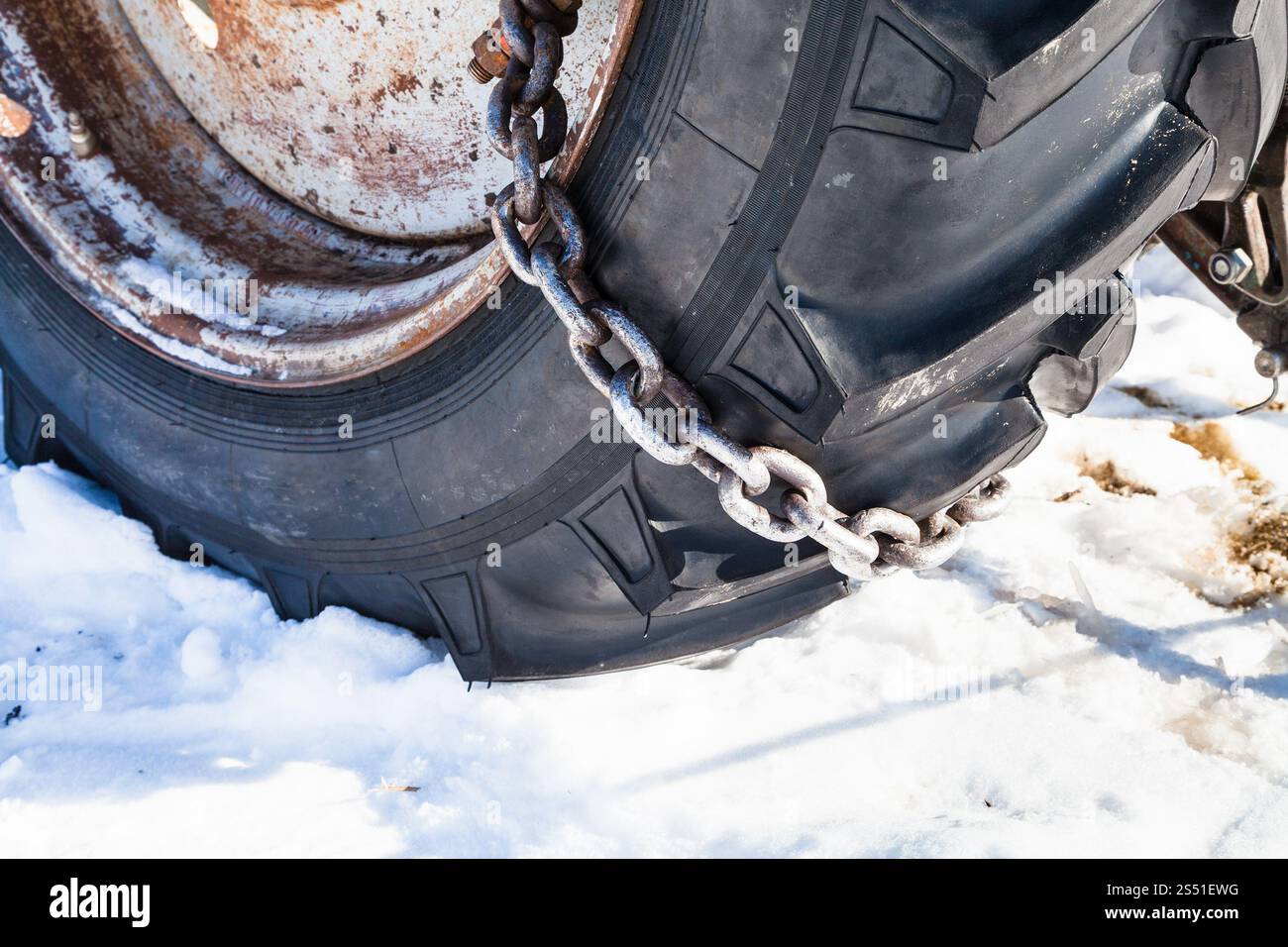 Chaîne à neige montée sur le pneu du tracteur. Chaîne à neige montée sur le pneu du tracteur sur route enneigée gros plan Banque D'Images