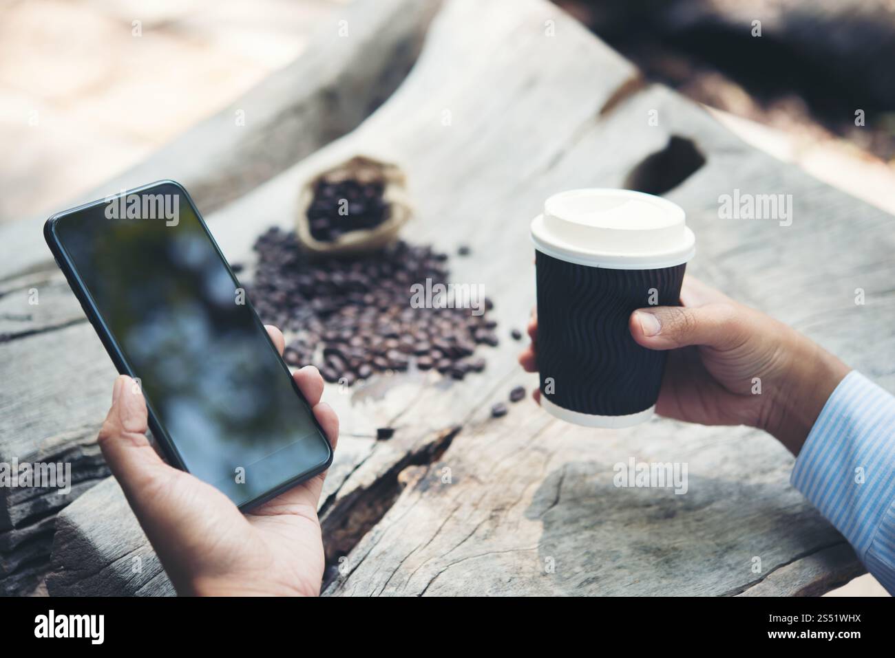 Main d'homme tenant la tasse de papier de café avec smartphone assis à . Main de l'homme tenant tasse de papier de café avec smartphone assis à la table en bois. Banque D'Images