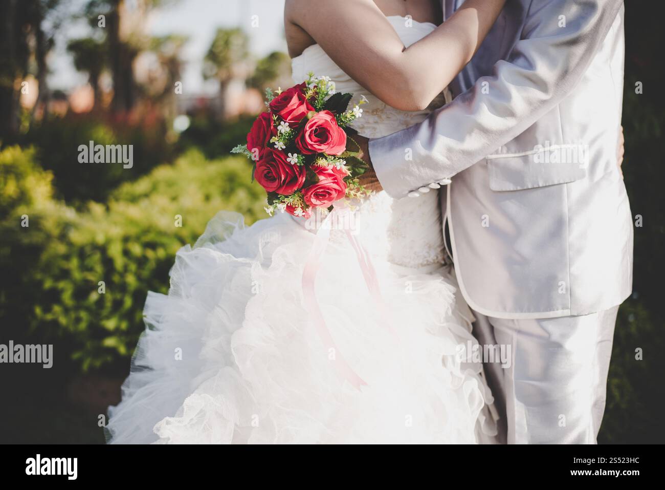 Mariée tient un bouquet de rose rouge de mariage dans les mains, les câlins du marié. Mariée tient un bouquet de rose rouge de mariage dans les mains, le marié embrasse sa mariée ensemble. Banque D'Images