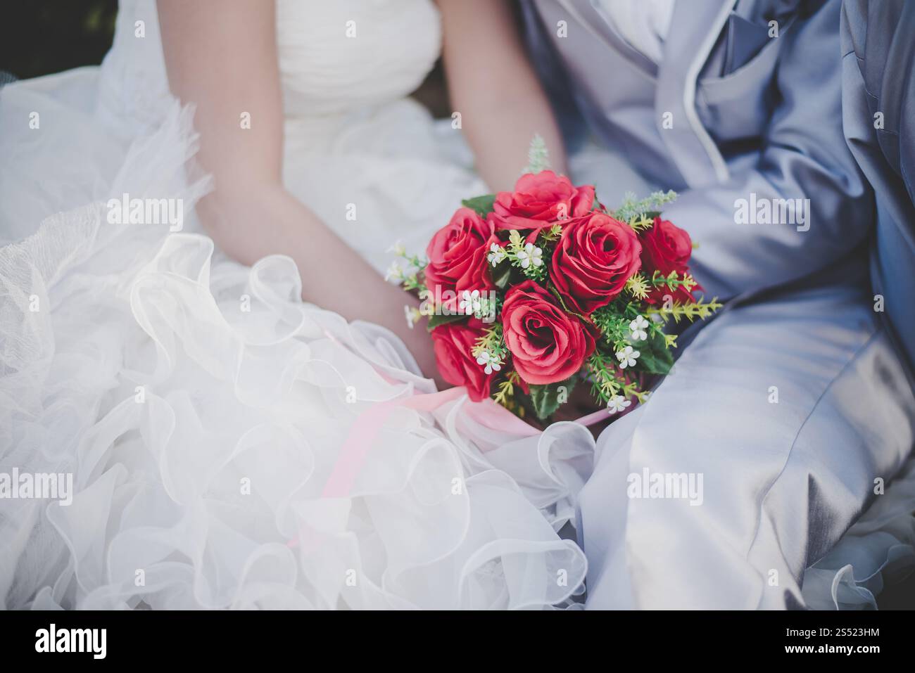 Mariée tient un bouquet de rose rouge de mariage dans les mains, les câlins du marié. Mariée tient un bouquet de rose rouge de mariage dans les mains, le marié embrasse sa mariée ensemble. Banque D'Images