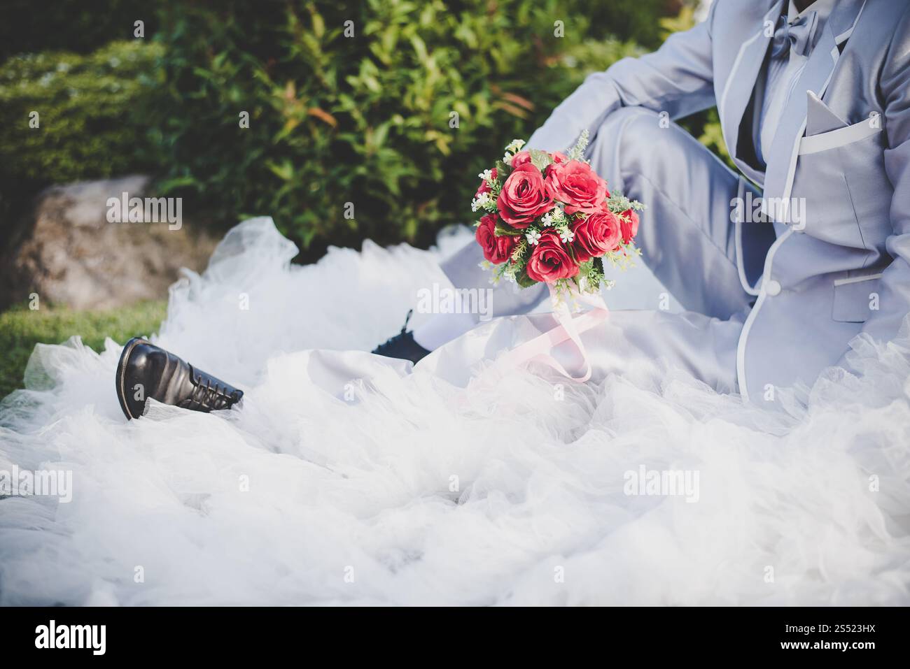 Mariée tient un bouquet de rose rouge de mariage dans les mains, les câlins du marié. Mariée tient un bouquet de rose rouge de mariage dans les mains, le marié embrasse sa mariée ensemble. Banque D'Images