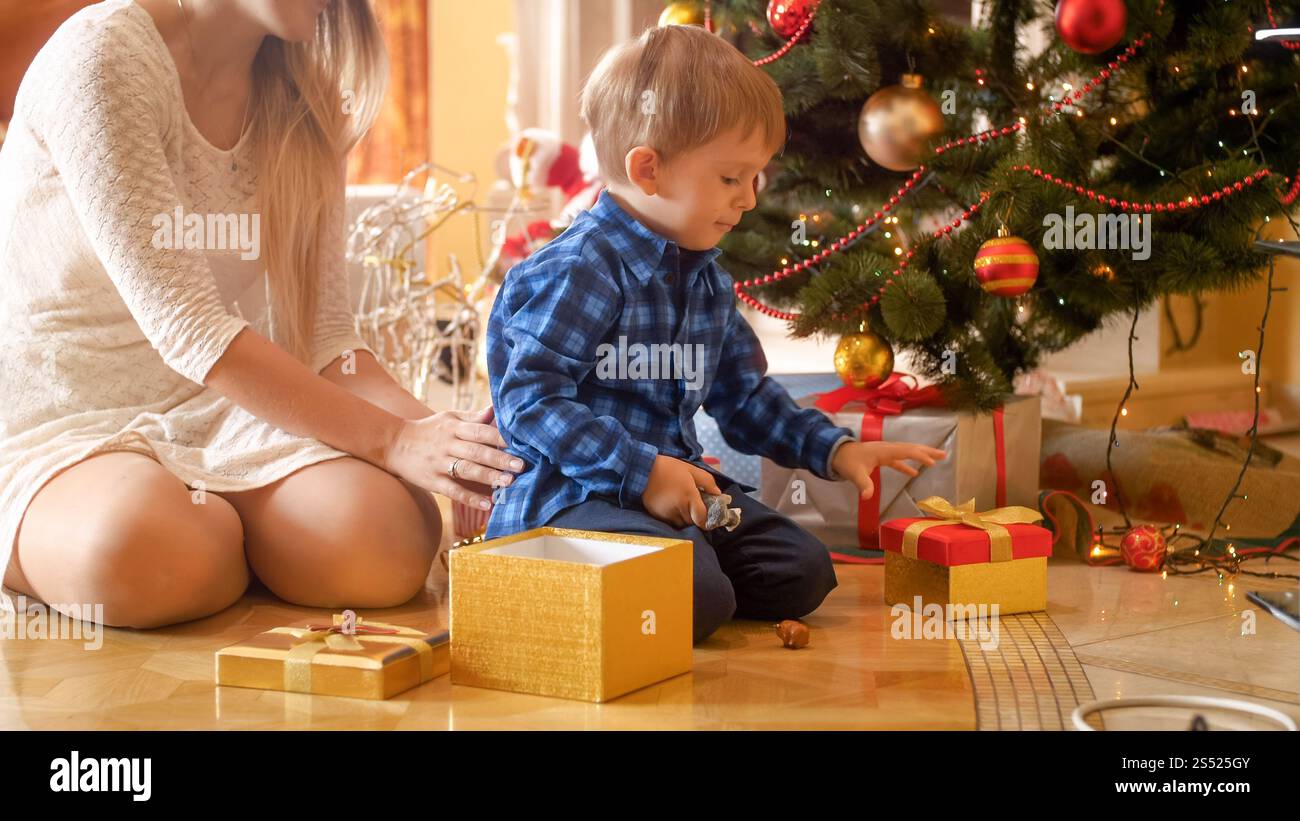 Le tout-petit garçon ouvre la boîte cadeau hristmas le matin au salon. Mignon petit garçon ouvre la boîte cadeau hristmas le matin au salon Banque D'Images