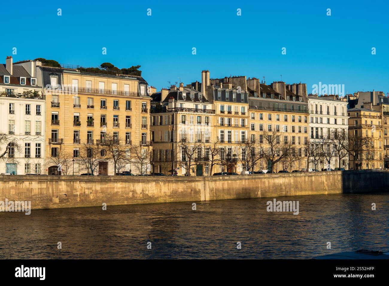Beaux bâtiments au bord de la rivière le long de l'eau calme sous un ciel bleu clair Banque D'Images