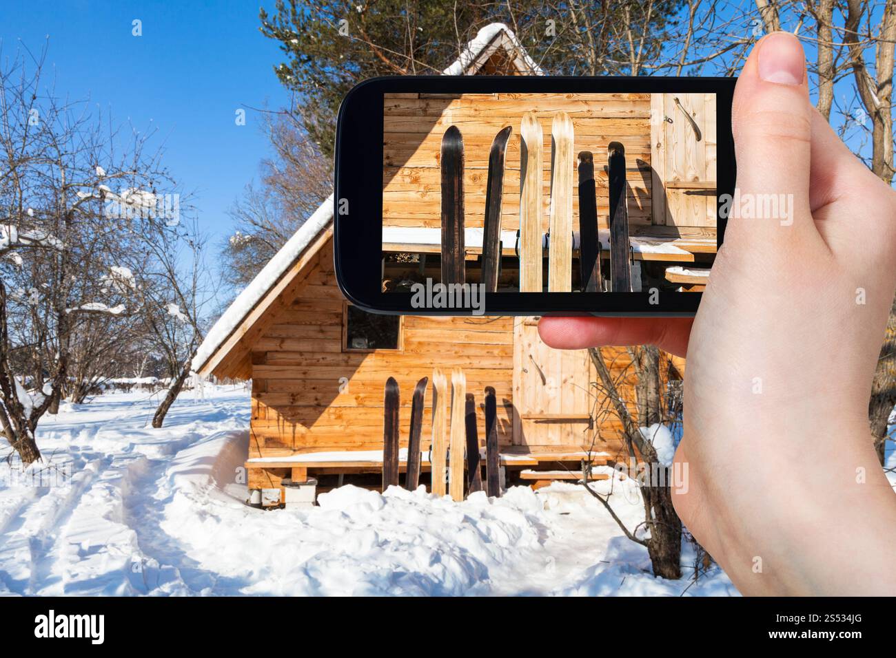 Travel Concept - photos touristiques de grande forêt skis en face de maison en bois en hiver ensoleillée journée sur smartphone dans la région de Smolensk Banque D'Images