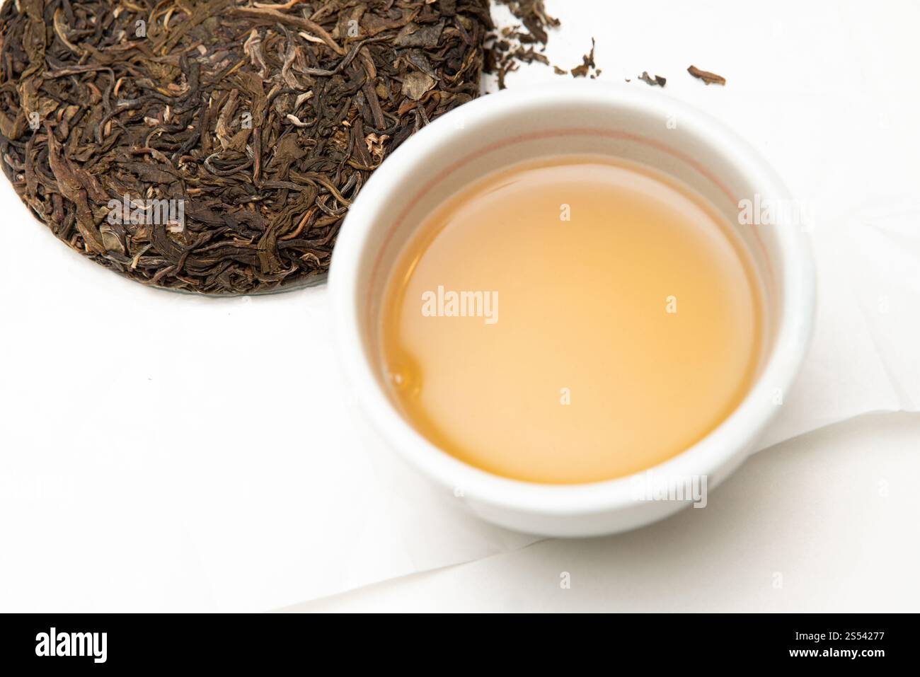 Bol en porcelaine Chawan avec thé sheng pu-erh fraîchement infusé. Gâteau de thé pu-erh cru pressé sur la table pleine de feuilles de thé vieillies. Véritable chef-d'œuvre artisanal Banque D'Images