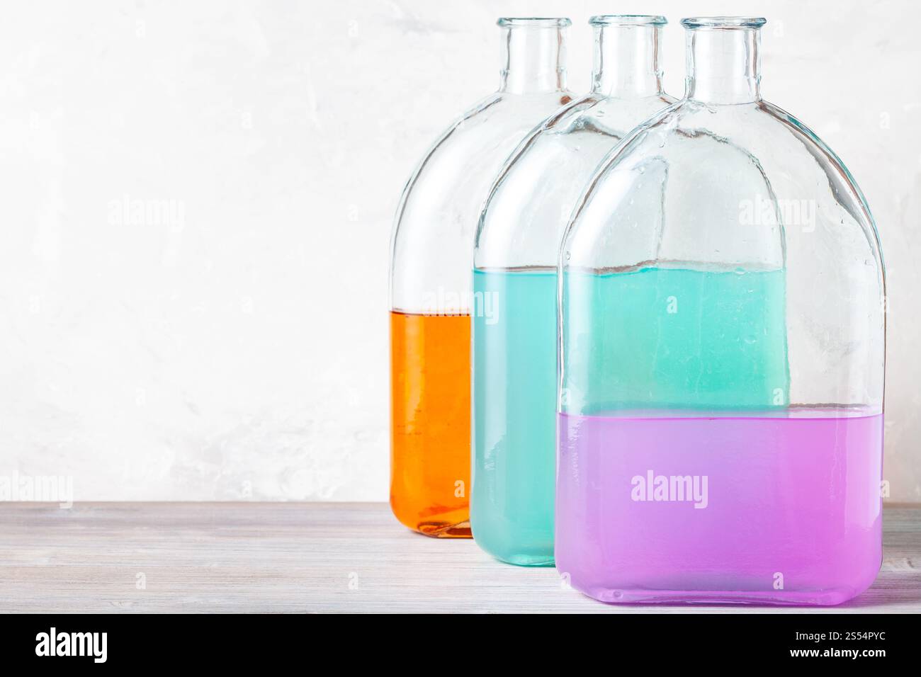 bouteilles en verre avec des solutions d'aquarelle de couleur sur panneau de bois gris près du mur de béton gris. bouteilles en verre avec des solutions d'aquarelle sur gris Banque D'Images