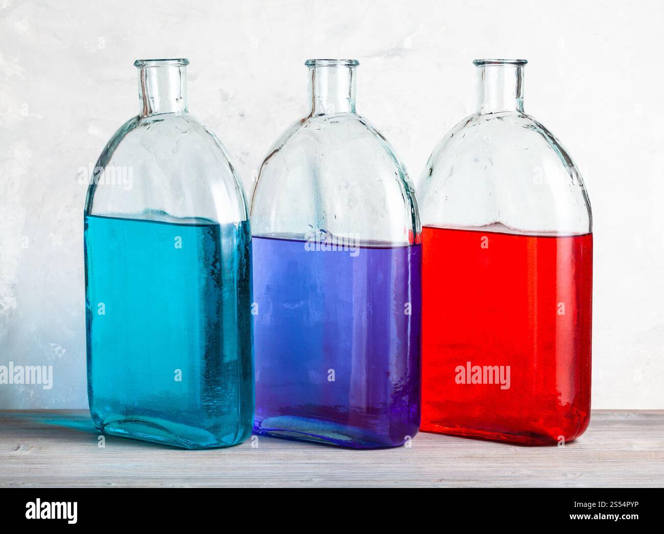 trois bouteilles avec des solutions d'encre de couleur sur panneau de bois gris près du mur de béton gris. trois bouteilles avec des solutions d'encre de couleur sur gris Banque D'Images