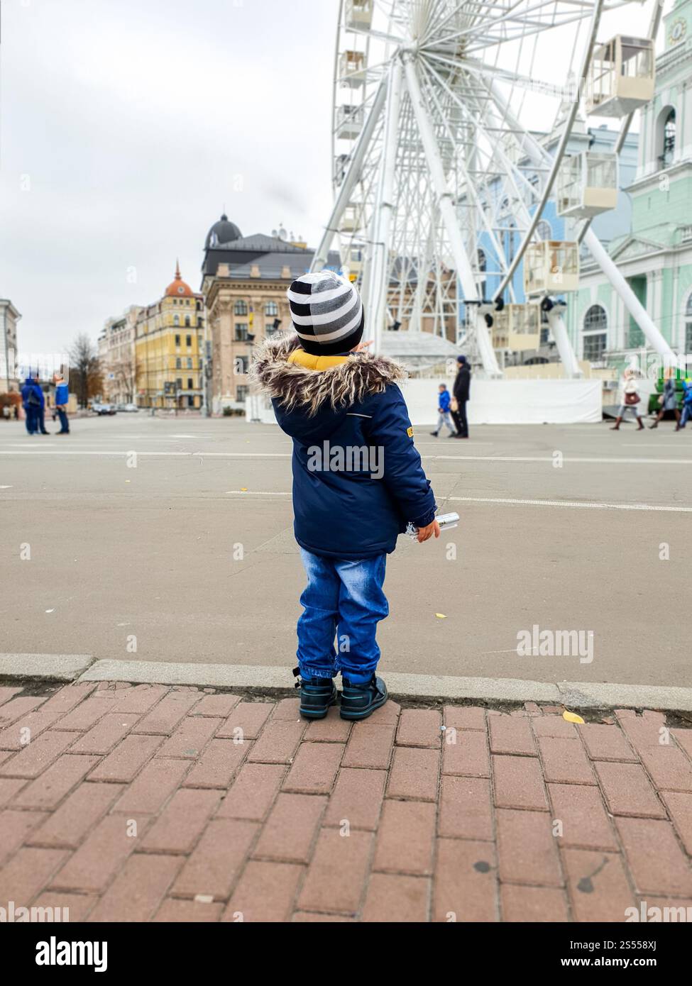 Image d'un jeune garçon de 3 ans regardant sur la grande roue de ferris sur la rue de la ville. Photo d'un garçon en bas âge de 3 ans regardant sur la grande roue Banque D'Images