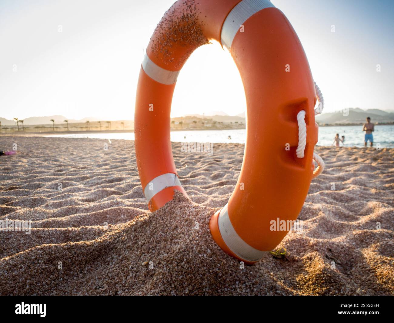 Gros plan image de l'anneau de sauvetage en plastique rouge sur le sable de la plage de la mer contre beau coucher de soleil sur l'océan. Gros plan photo de la vie en plastique rouge Banque D'Images