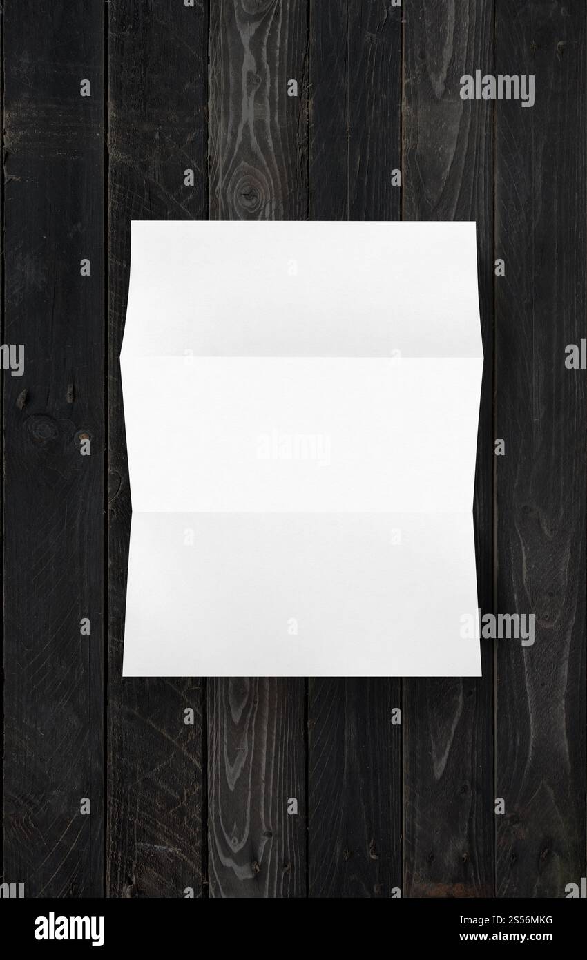 Modèle de maquette de feuille de papier A4 blanc plié vierge isolé sur fond de bois noir. Modèle de maquette de feuille de papier A4 blanc plié vierge sur bois noir Banque D'Images