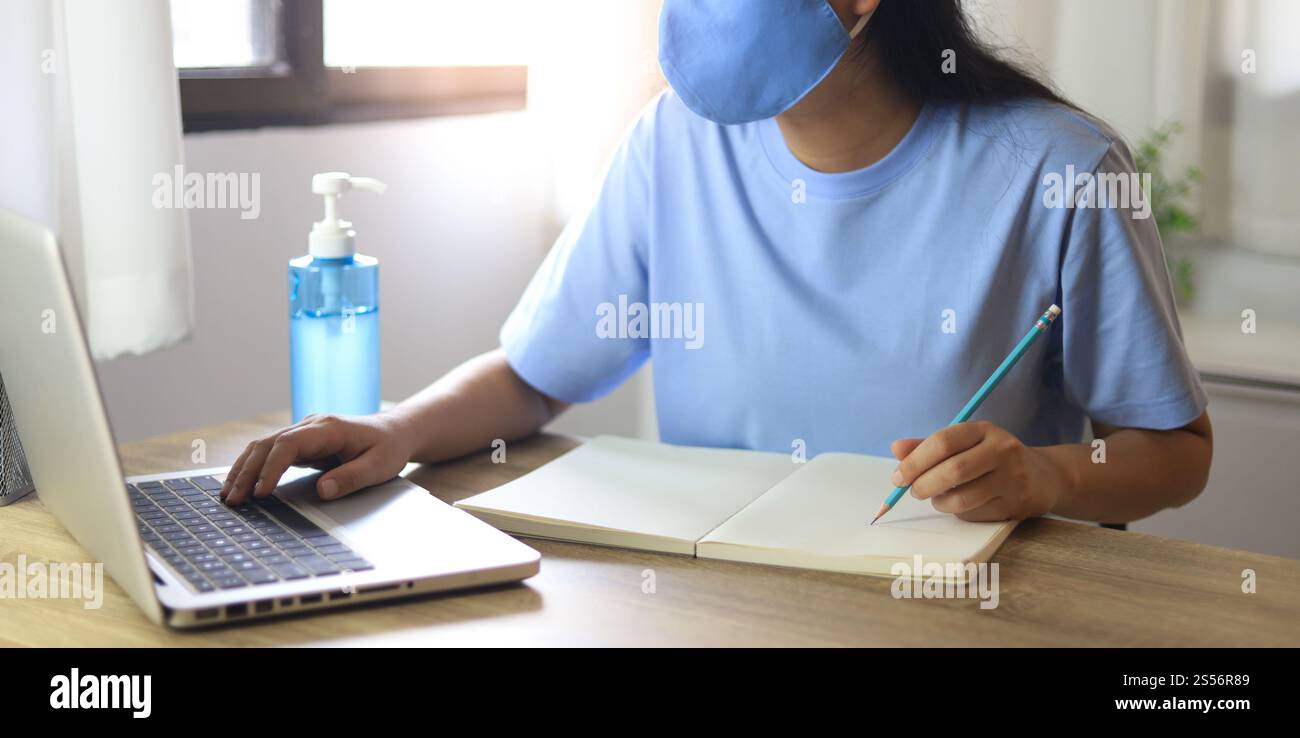 Jeune femme asiatique portant le masque médical fait à la main du visage travaillant seule politique de distanciation avec. Gel désinfectant pour les mains pendant le coronavirus ou le virus covid-19 Banque D'Images