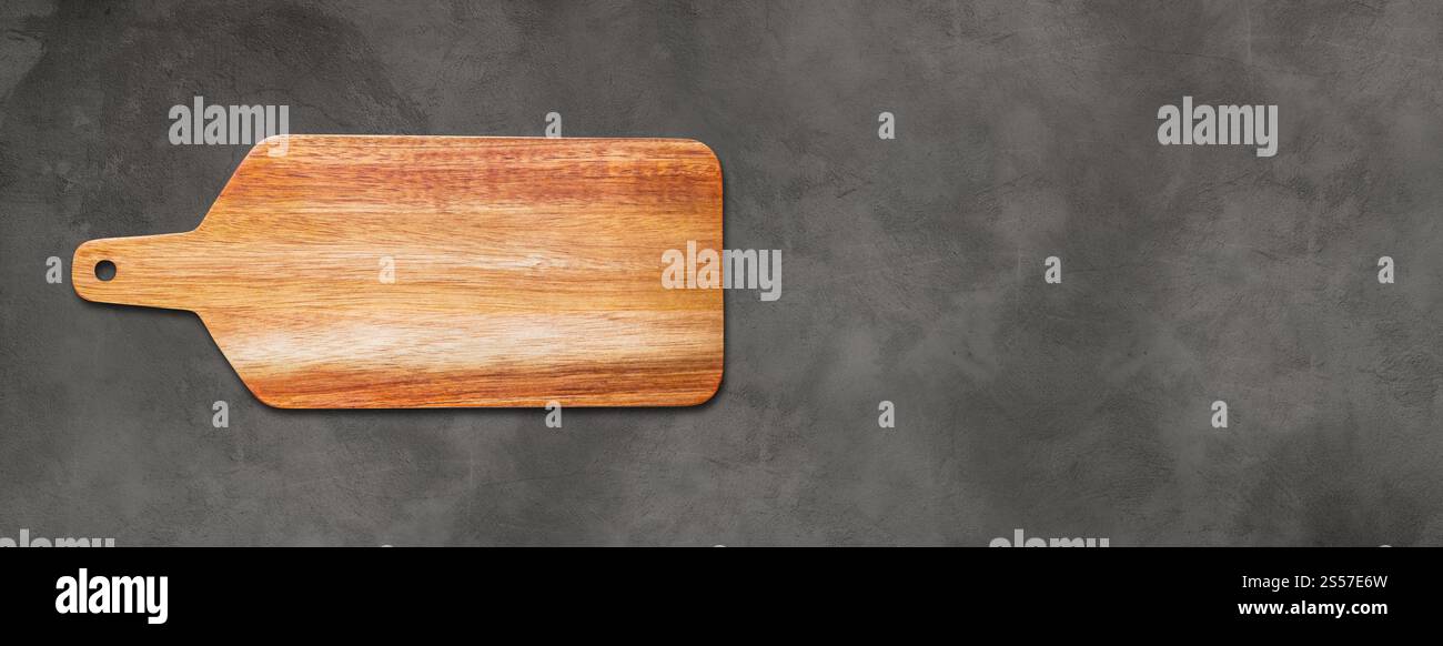 Planche à découper en bois isolé sur fond de béton foncé. Bannière panoramique horizontale. Planche à découper en bois isolé sur fond de béton foncé. Banque D'Images