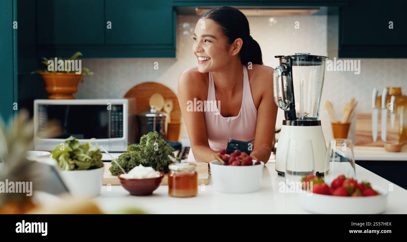 Téléphone, pensée et femme avec smoothie dans la cuisine pour la santé, le bien-être et le petit déjeuner diététique. Heureux, idée et personne féminine avec téléphone portable pour la nutrition Banque D'Images
