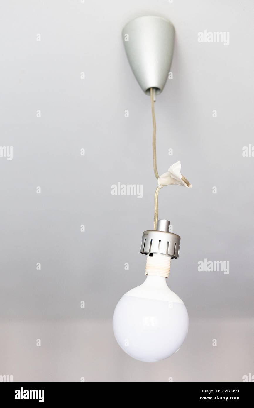 La lampe LED en forme de boule est suspendue sur des fils enveloppés dans du ruban adhésif à la maison Banque D'Images