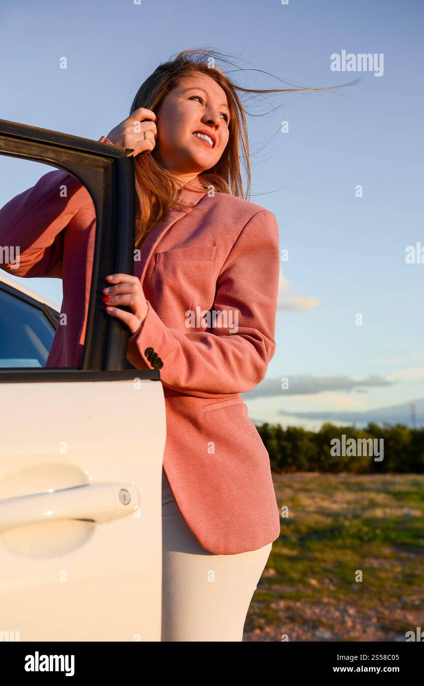 Jeune femme d'affaires sortant de la voiture, profitant du coucher du soleil lors d'un voyage en voiture relaxant dans la campagne Banque D'Images