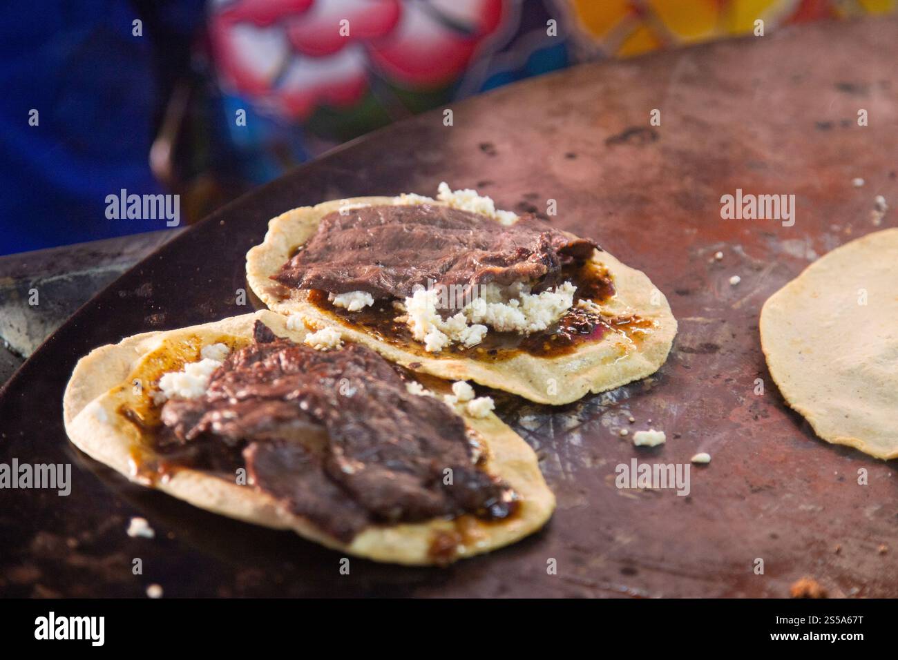 Cuisson de memelas au marché d'Oaxaca Central de Abastos avec fromage local, porc séché, œufs et sauce piquante. Banque D'Images