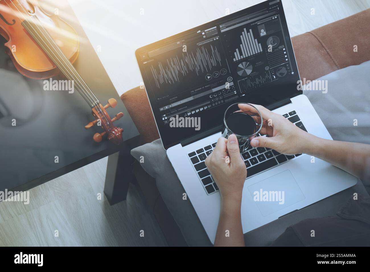 Hipster main tenant une tasse de café pendant la composition de la musique avec ordinateur portable compter et sitting on sofa at home studio Banque D'Images
