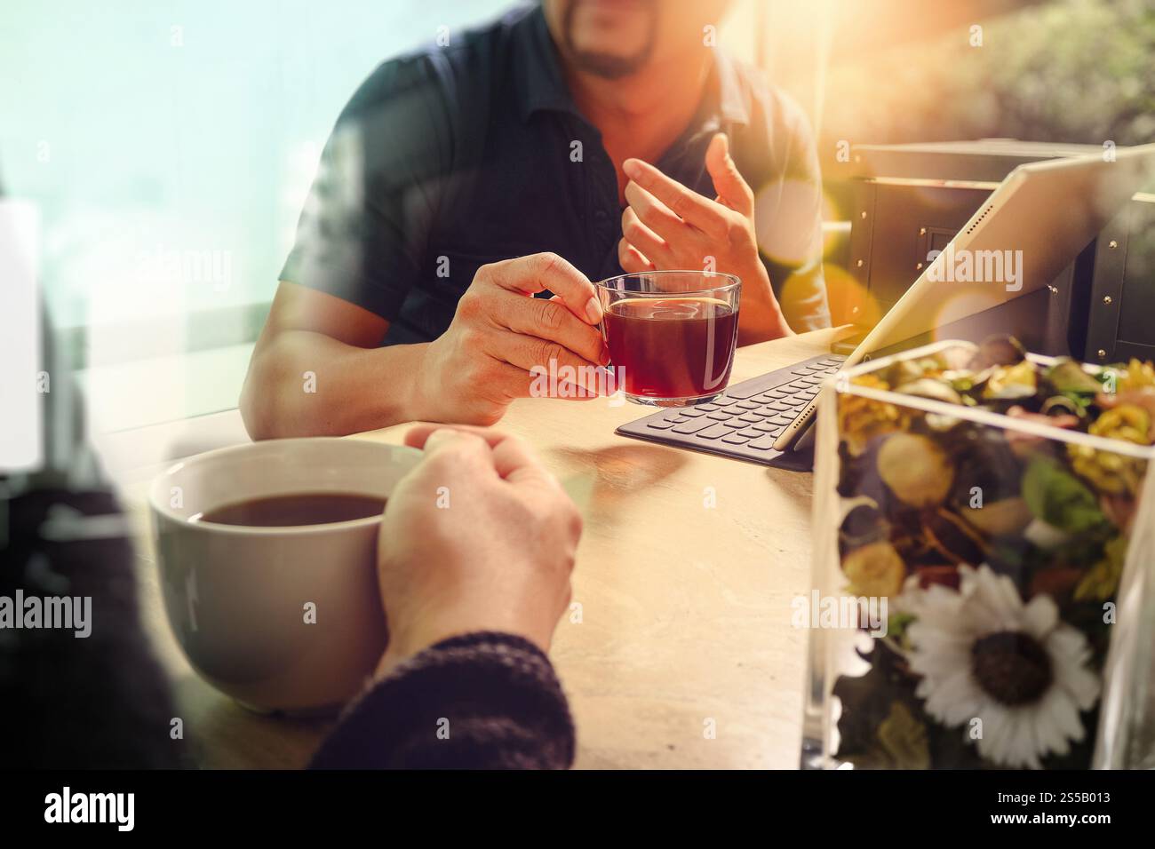Pause café de bureau avec deux collègues de concepteur assis discutant sur des tasses de café, vase de fleurs, tablette numérique amarrage clavier intelligent sur marbre Banque D'Images