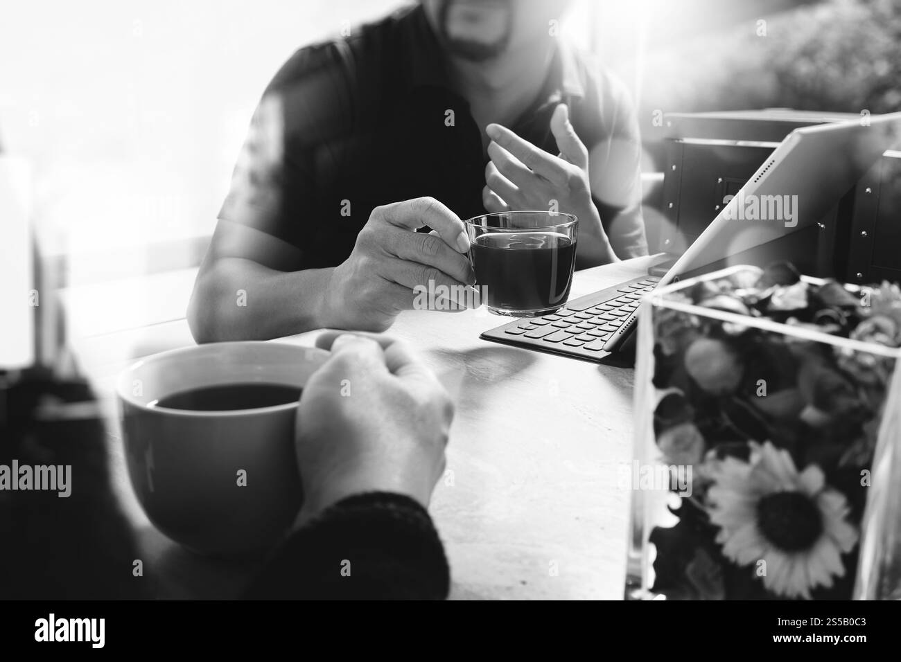 Pause café de bureau avec deux collègues de concepteur assis discutant sur des tasses de café, vase de fleur, tablette numérique amarrant clavier intelligent sur marbre Banque D'Images
