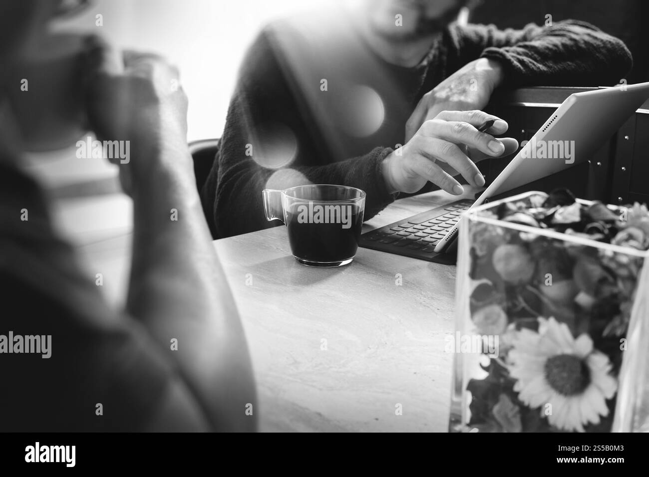 Pause café de bureau avec deux collègues de concepteur assis discutant sur des tasses de café, vase de fleur, tablette numérique amarrant clavier intelligent sur marbre Banque D'Images