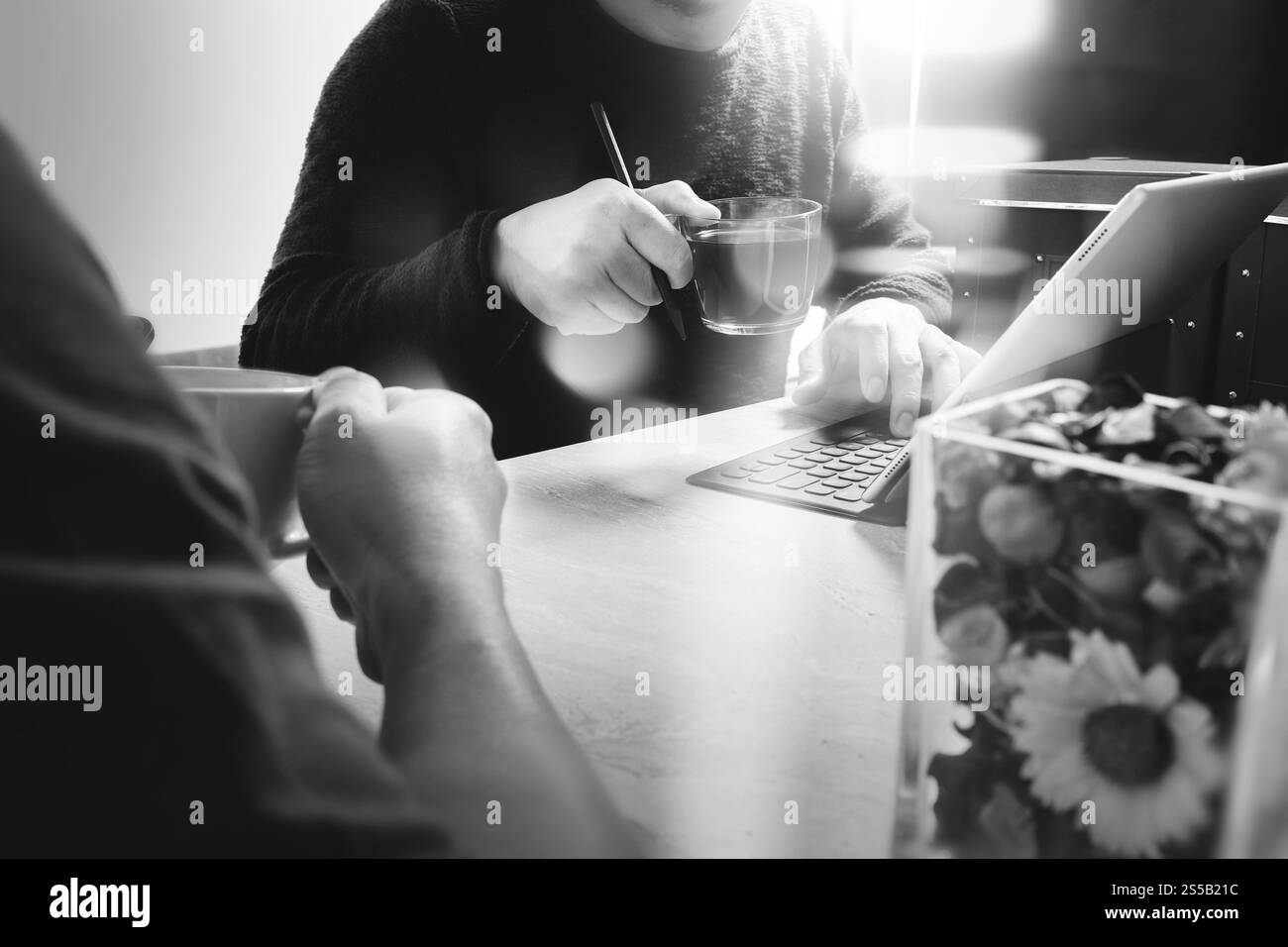 Pause café de bureau avec deux collègues de concepteur assis discutant sur des tasses de café, vase de fleur, tablette numérique amarrant clavier intelligent sur marbre Banque D'Images