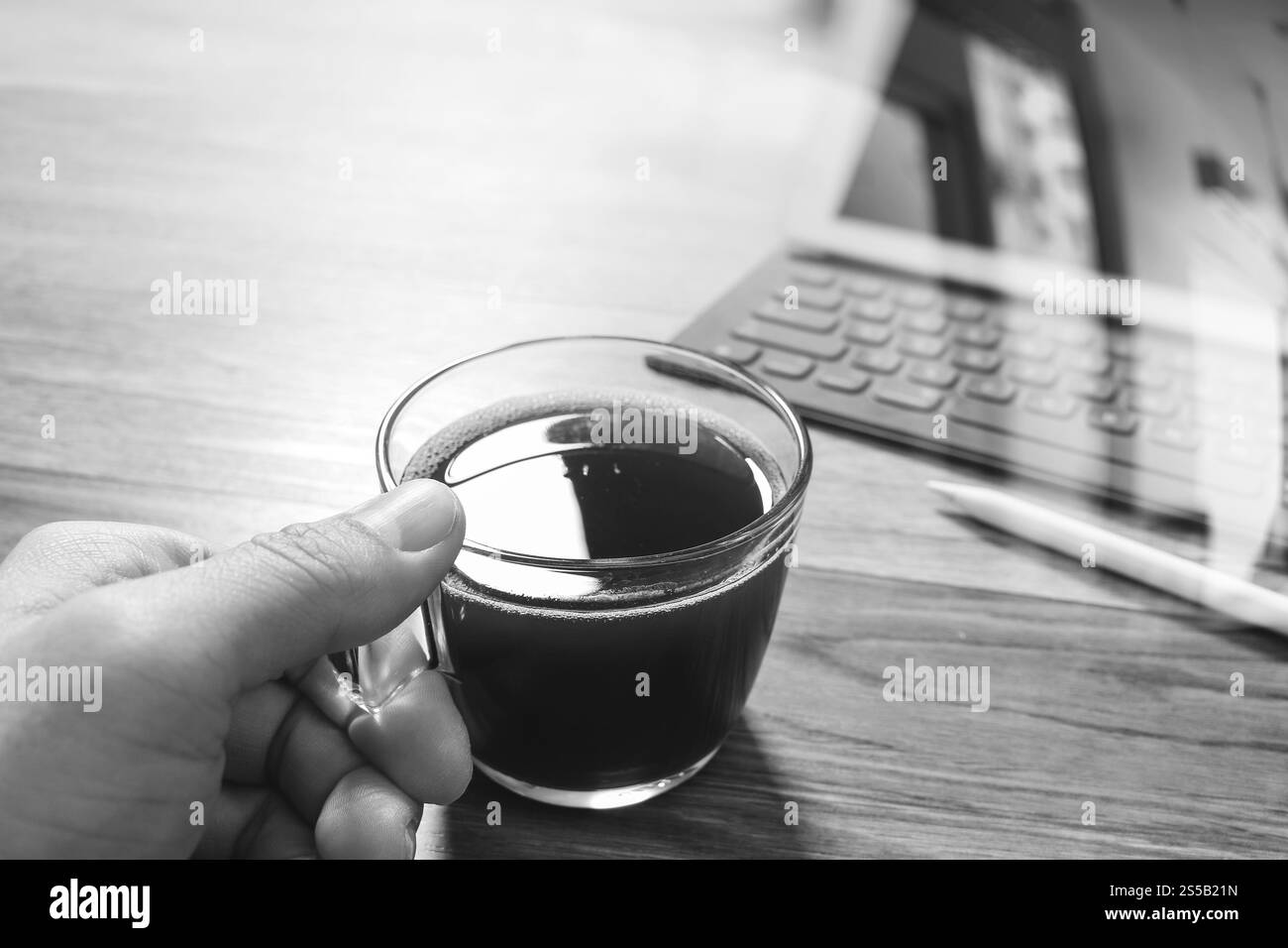 Main tenant une tasse à café ou thé et table numérique dock clavier smart,stylet sur table en bois,blanc,noir effet filtre Banque D'Images