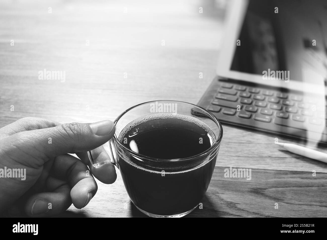 Main tenant une tasse à café ou thé et table numérique dock clavier smart,stylet sur table en bois,blanc,noir effet filtre Banque D'Images