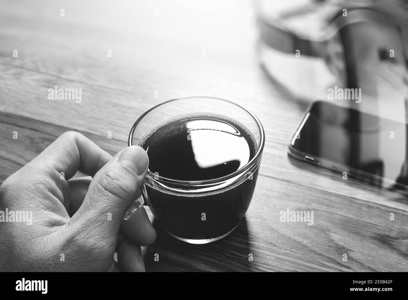 Main tenant une tasse à café ou thé et casque voip,smart phone sur table en bois,filtre,black white Banque D'Images