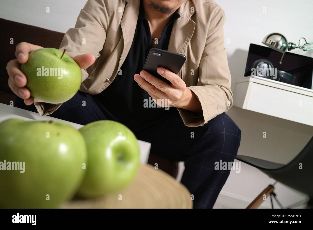 Hipster la main à l'aide de smart phone pour les paiements mobiles les entreprises en ligne, sitting on sofa in living room,holding green apple en plateau en bois Banque D'Images
