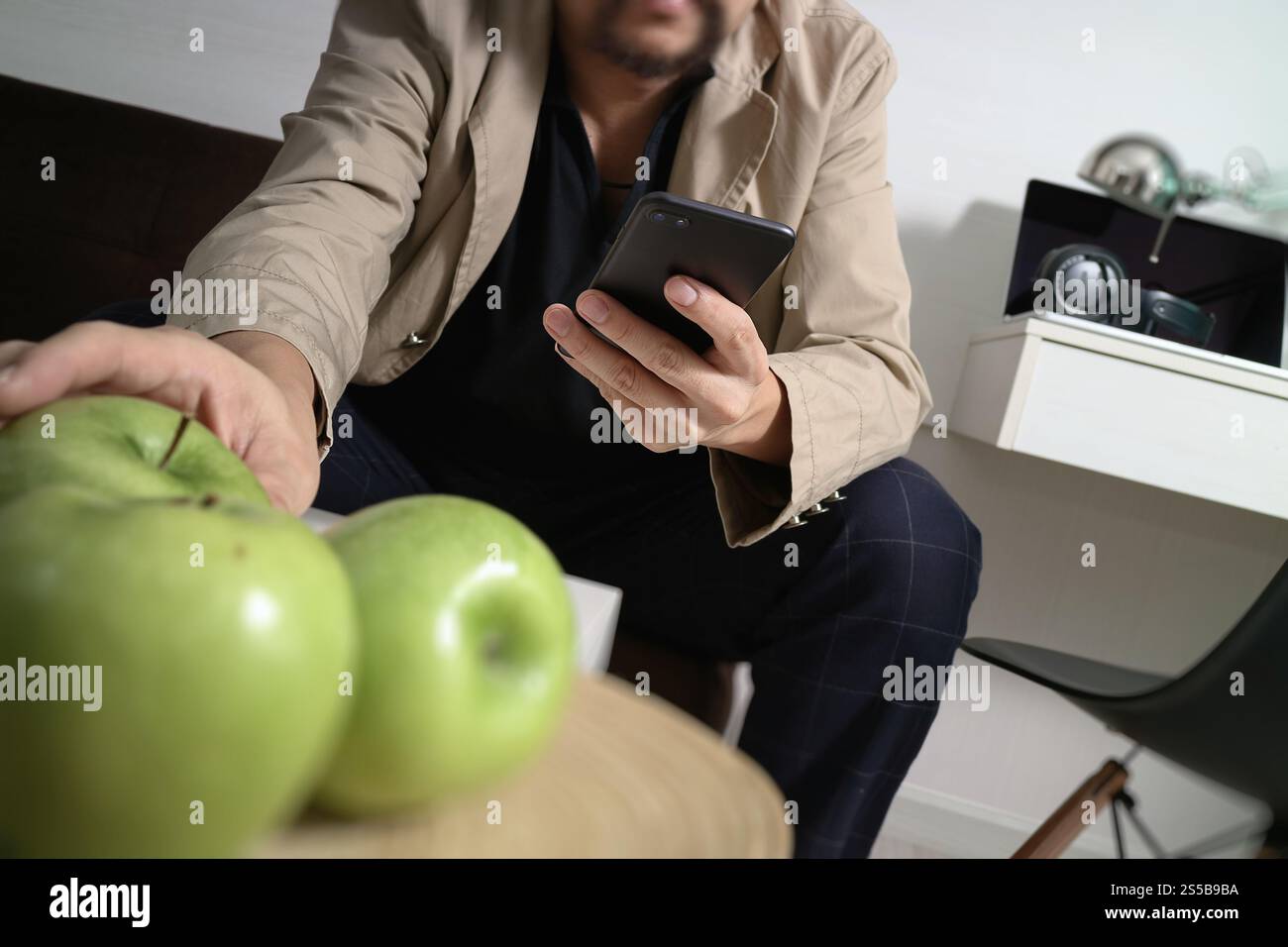 Hipster la main à l'aide de smart phone pour les paiements mobiles les entreprises en ligne, sitting on sofa in living room,holding green apple en plateau en bois Banque D'Images