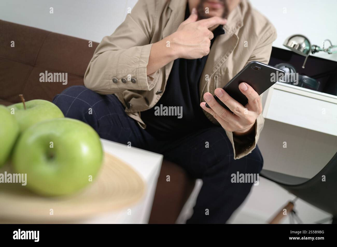 Hipster la main à l'aide de smart phone pour les paiements mobiles les entreprises en ligne, sitting on sofa in living room,holding green apple en plateau en bois Banque D'Images