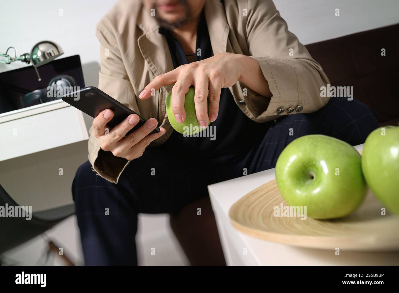 Hipster la main à l'aide de smart phone pour les paiements mobiles les entreprises en ligne, sitting on sofa in living room,holding green apple en plateau en bois Banque D'Images