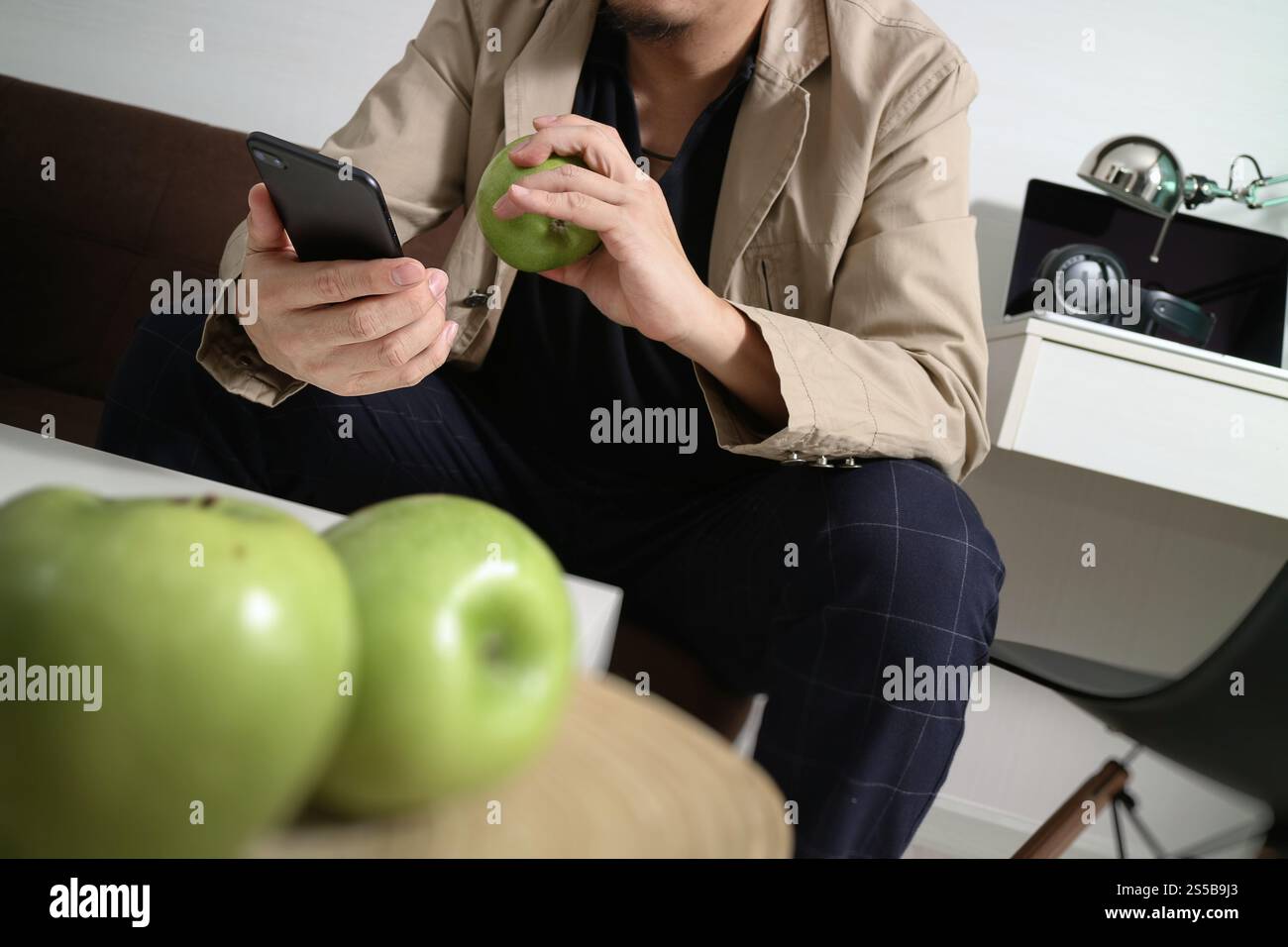 Hipster la main à l'aide de smart phone pour les paiements mobiles les entreprises en ligne, sitting on sofa in living room,holding green apple en plateau en bois Banque D'Images